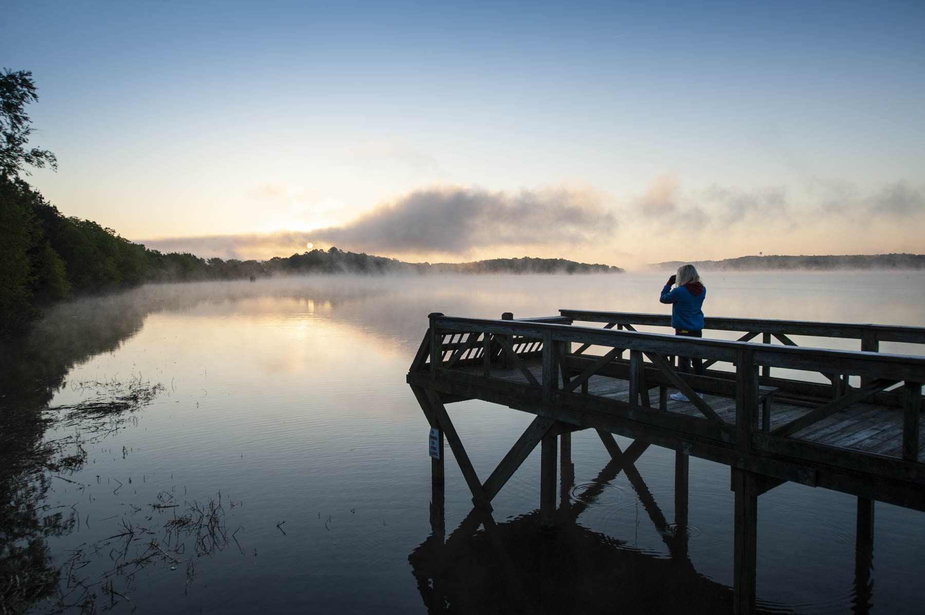 A woman looks out over Beaverfork Lake at dawn in Conway, AR