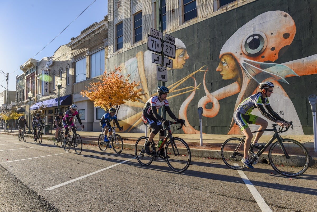 Cyclists riding by a mural