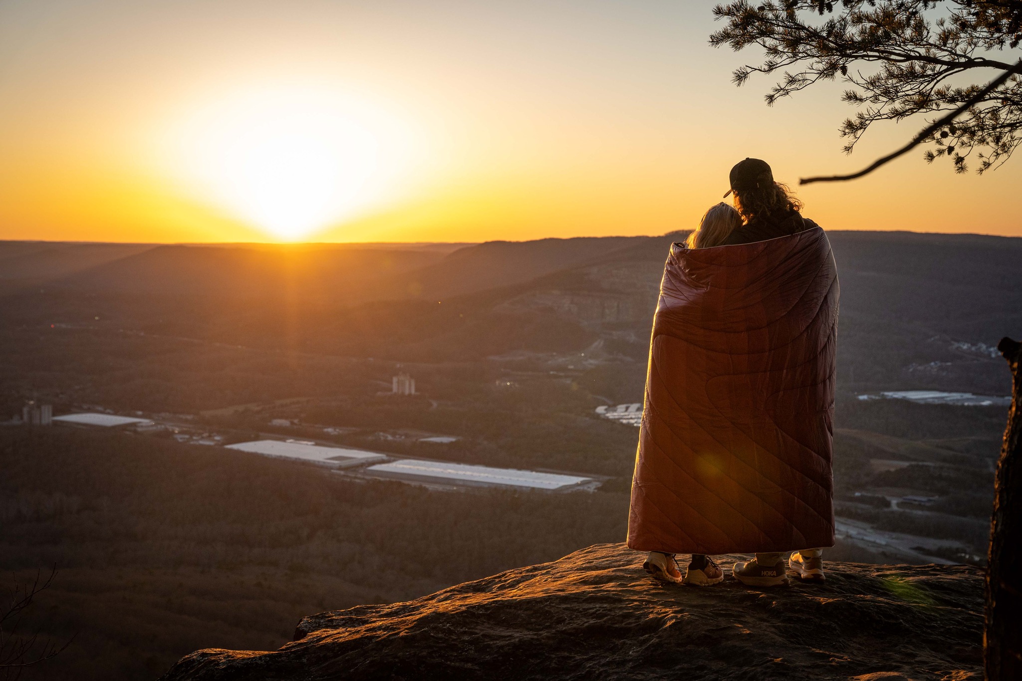 Two people wrapped in a blanket over looking the sunset from atop a mountain in Arkansas.