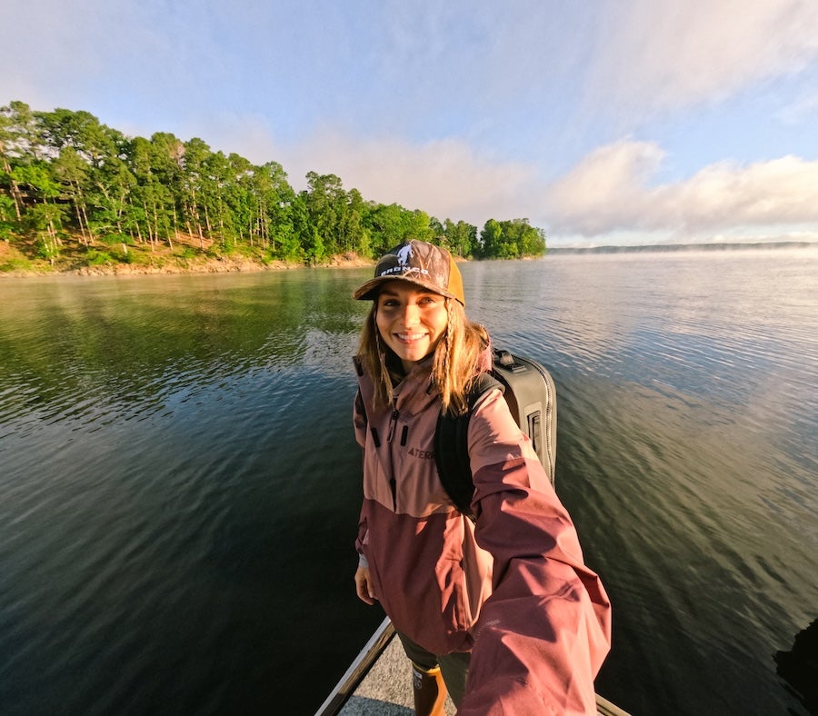 woman on Lake Ouachita in a boat taking a selfie with the sunset 