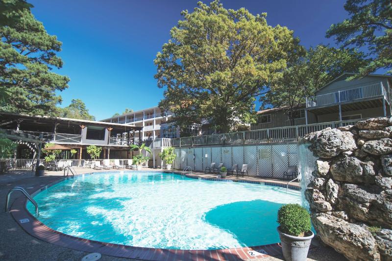 A kidney-shaped pool with blue water is surrounded by a concrete area with chaise loungers. Hotel room entrances can be seen beyond the loungers. 