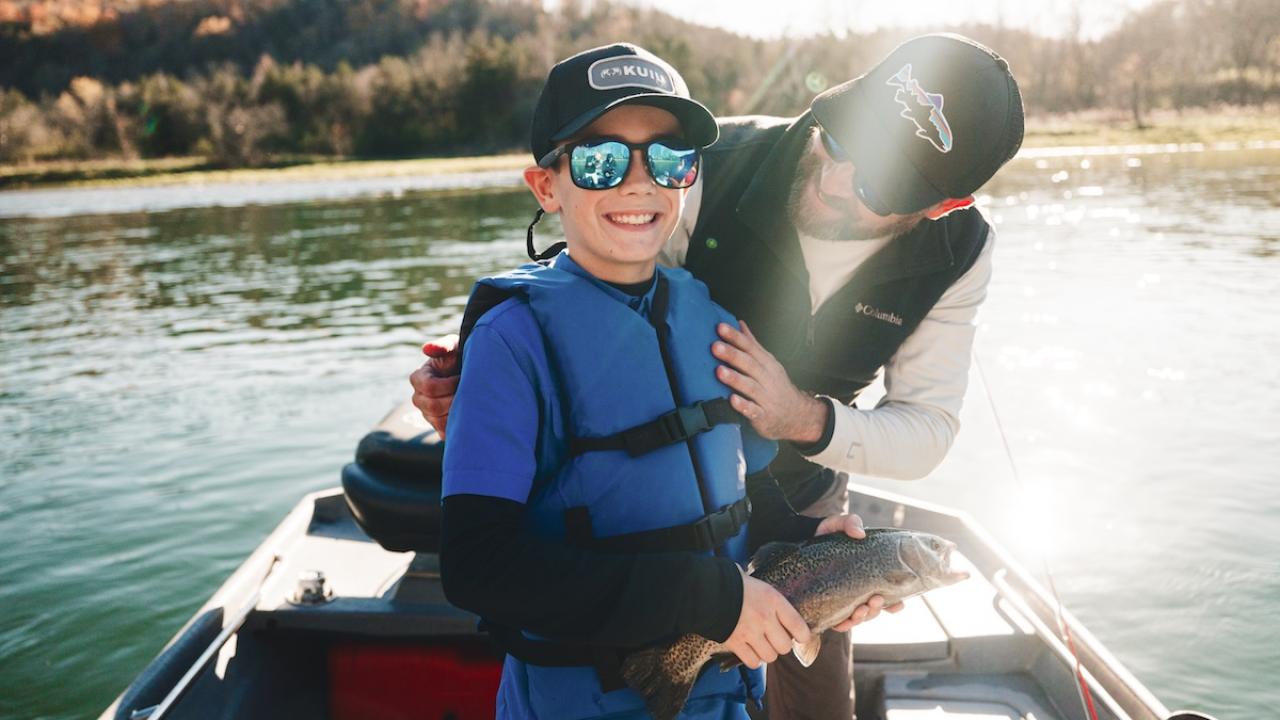father and son fishing off a boat on the river