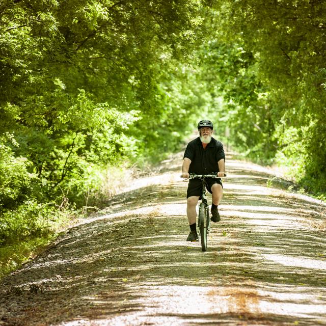 Cyclists cruises on the shaded gravel bike trail in Delta Heritage State Park