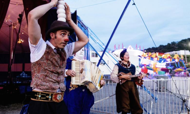Performers outside the Piccolo Zoppe Circus playing music and interacting with the crowd. 