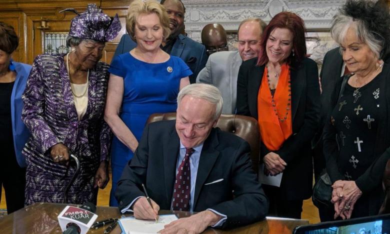 Governor Asa Hutchinson signs SB75, surrounded by Johnny Cash's daughter Rosanne and sister Joanne, and the goddaughter of Daisy Bates