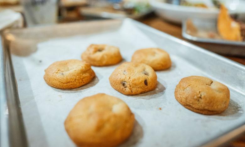 A dinner table. The background of a person and tall drink glasses is blurred. An individual-serving-size tray holds miniature chocolate chip cookies. Photo source: James Moore.