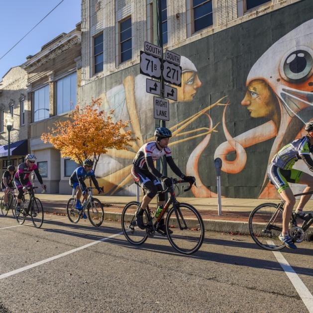 Cyclists riding by a mural