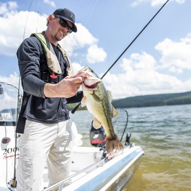 man holding up a fish on a boat on the lake