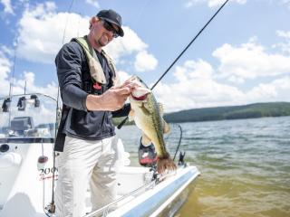 man holding up a fish on a boat on the lake