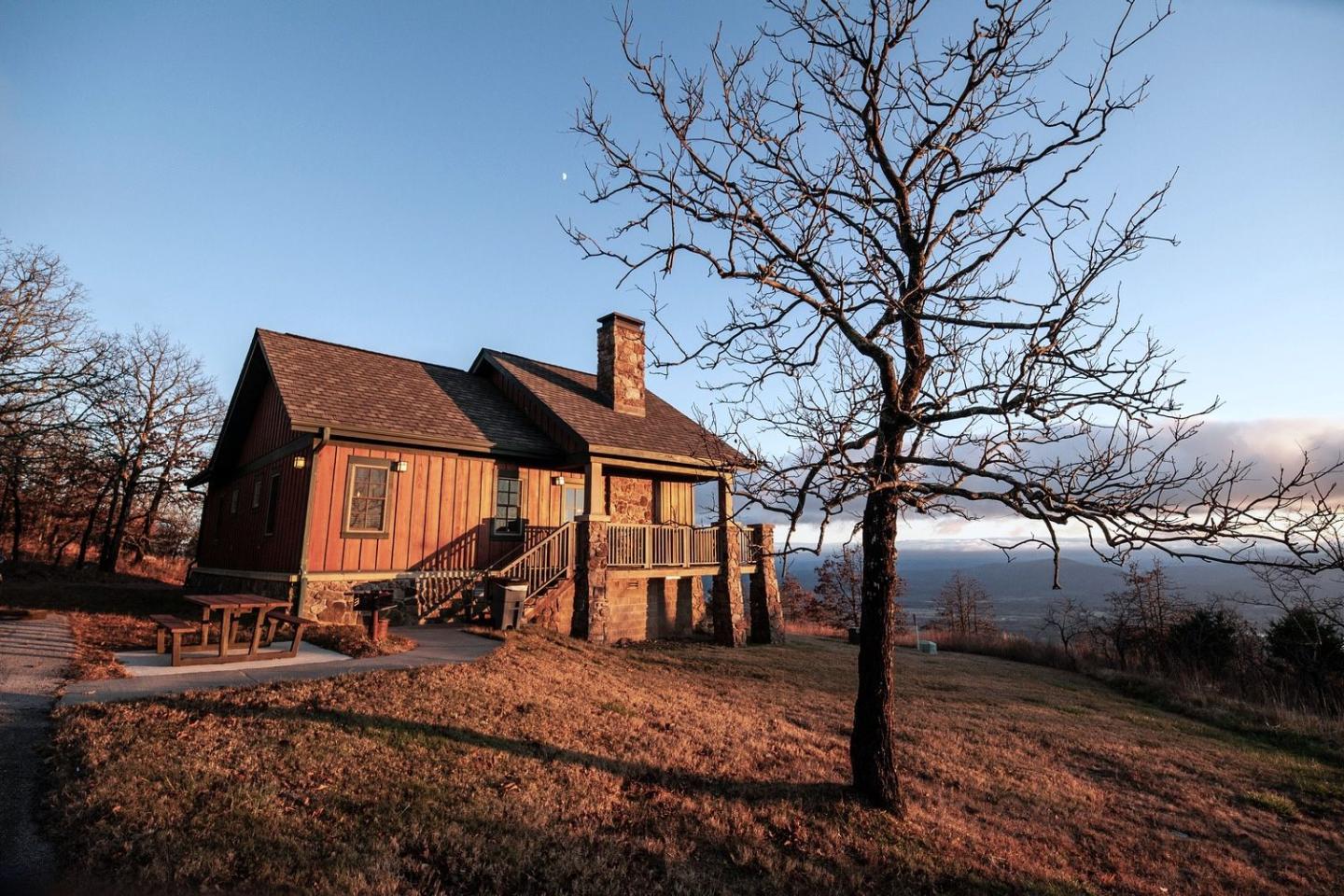 Wooden cabin at sunset with bare trees and orange grass.