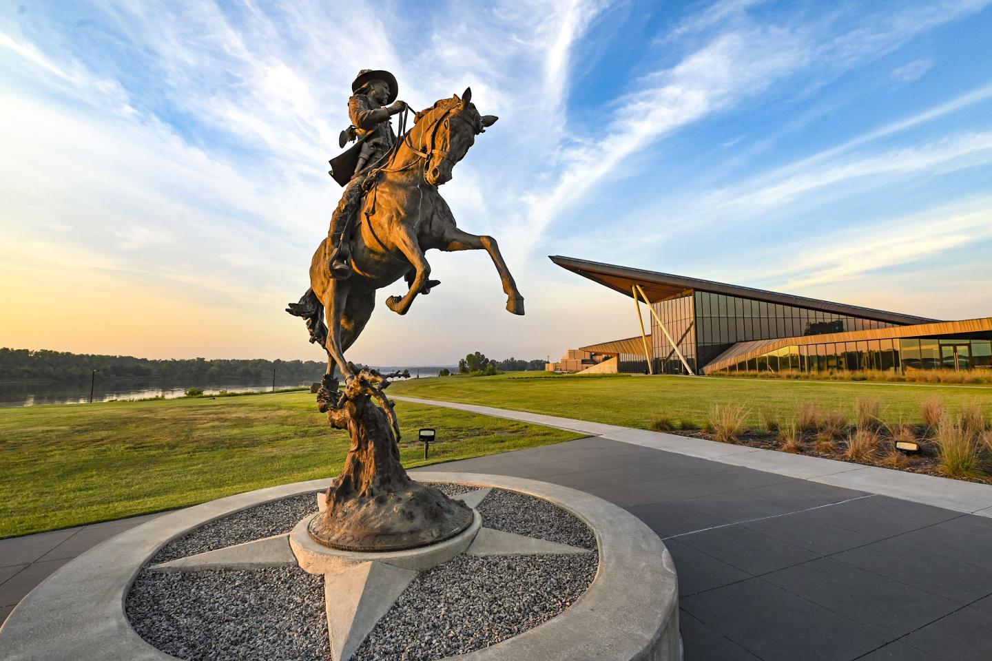 Bronze horse rider statue against a modern building and blue sky.