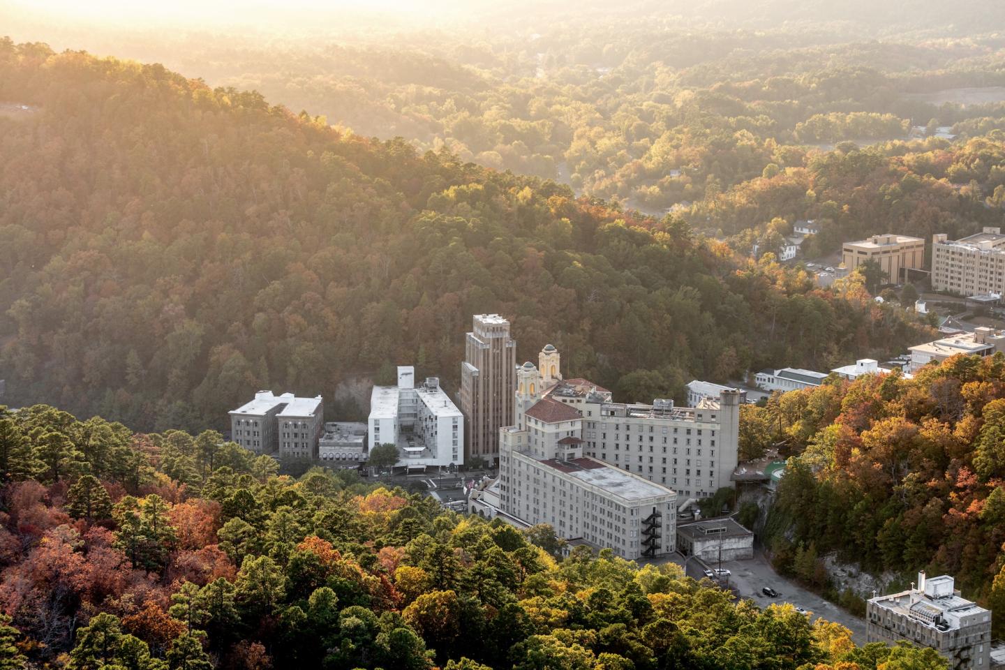 Aerial view of a hillside city at sunrise, surrounded by lush trees.
