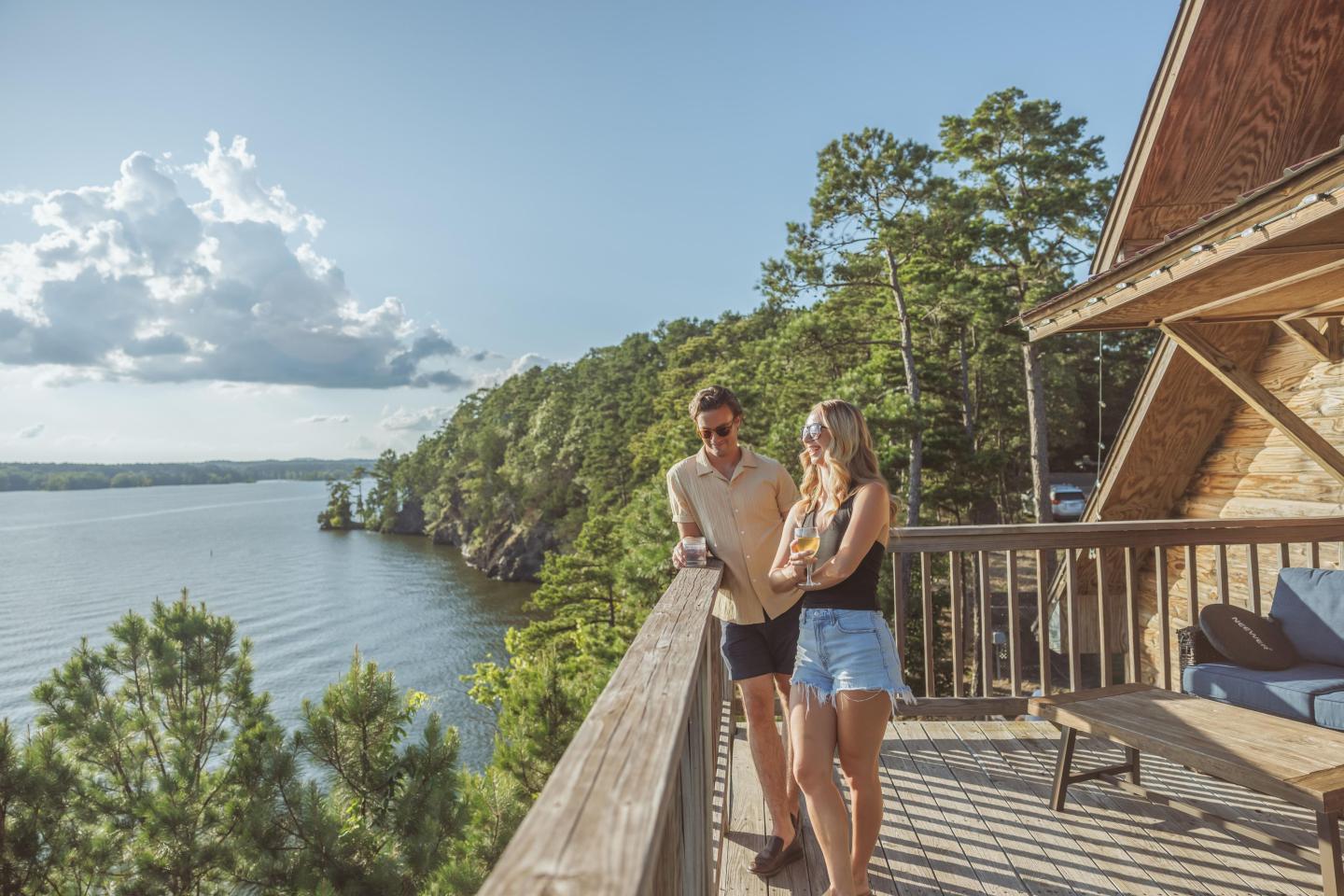 Couple on a wooden deck overlooking a lake, surrounded by trees.