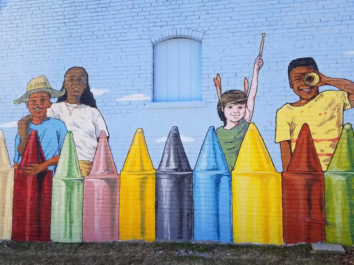 Children painted on a brick wall with large colorful crayon shapes.