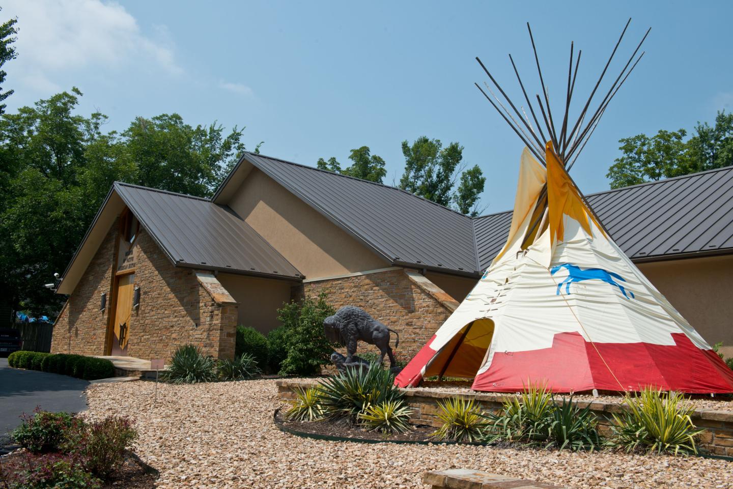Teepee with colorful horse design next to a modern building, under a blue sky.