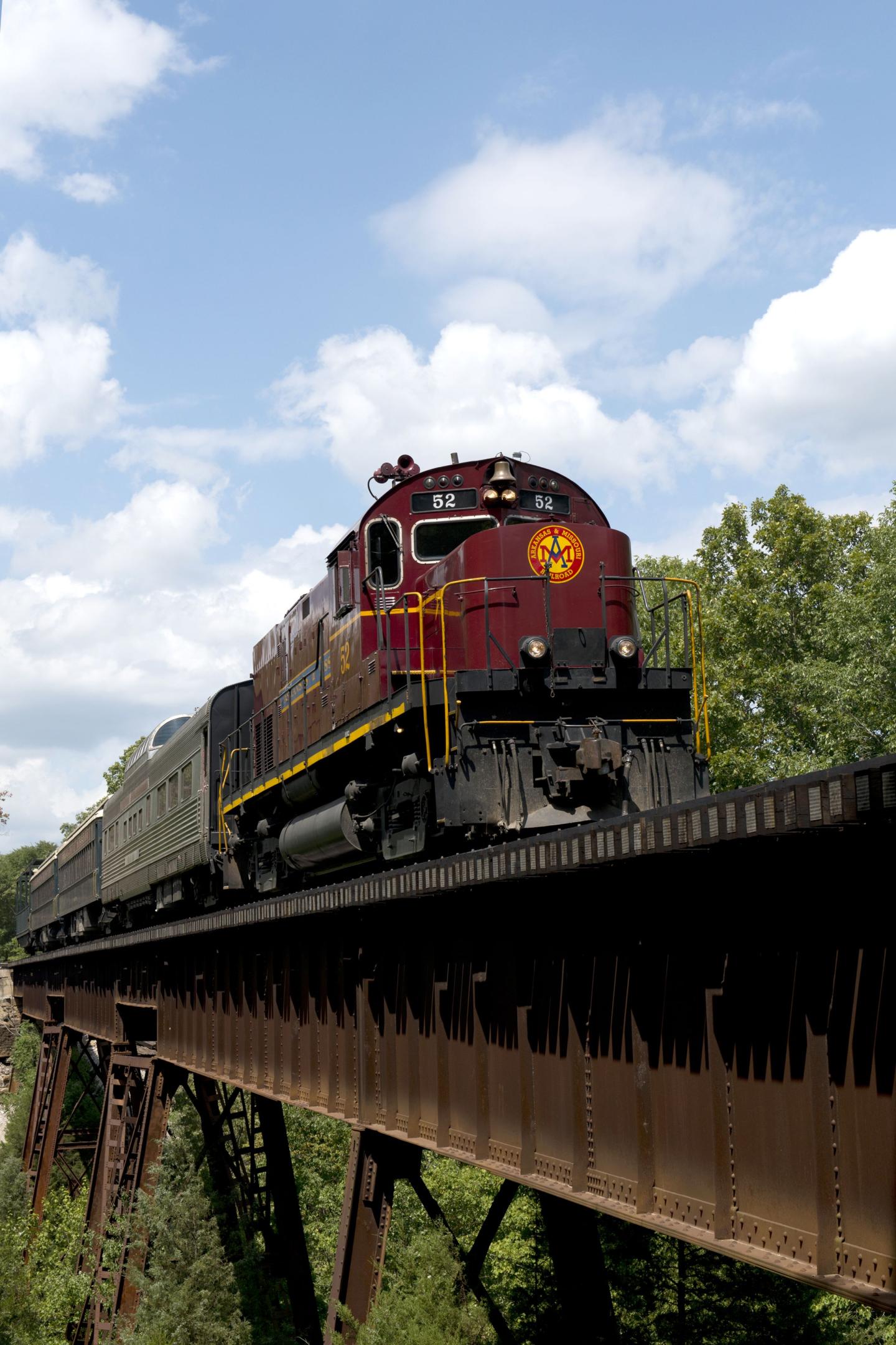 Red train crossing a tall bridge on a sunny day.