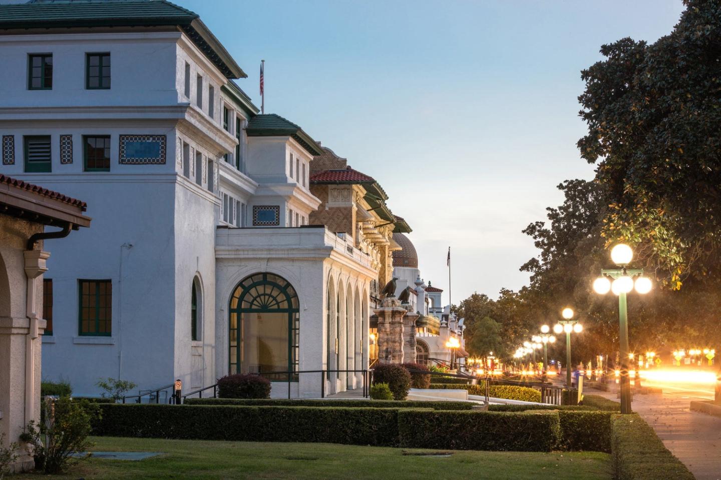 Historic buildings line a tree-lit street at dusk.