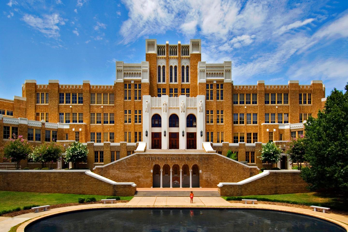 Large brown building with white accents, steps, and a reflecting pool, under a blue sky.