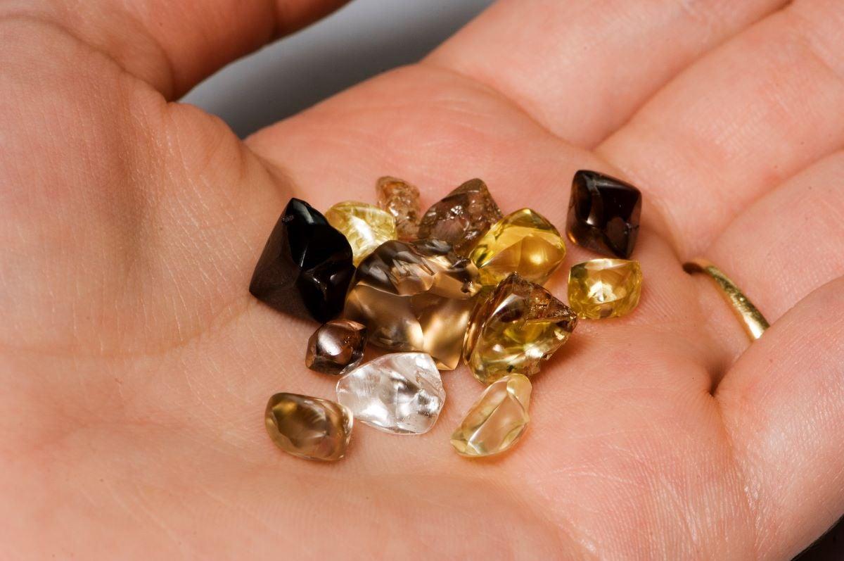 Hand holding various uncut gemstones in different colors.