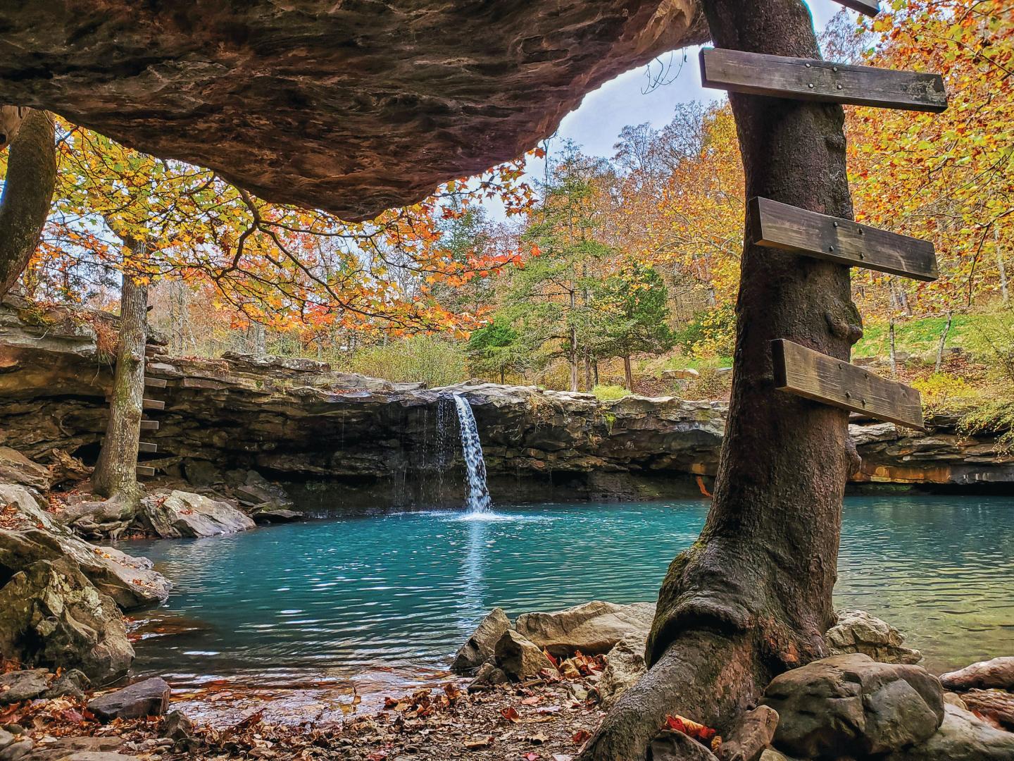 Waterfall flowing into a turquoise pool, surrounded by autumn trees.