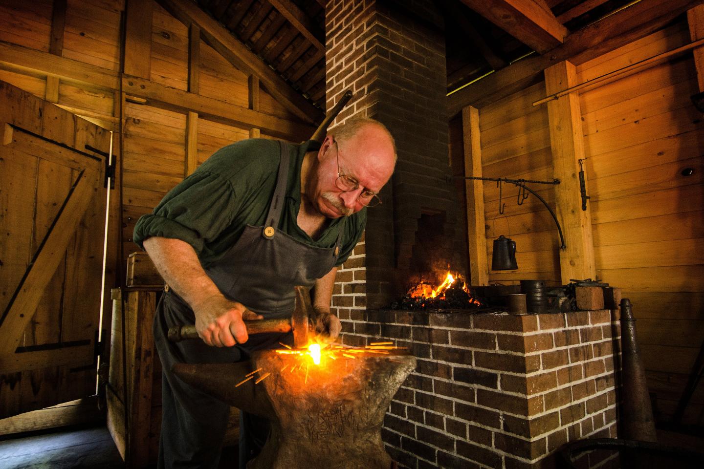 Blacksmith working with an anvil in a wooden workshop.