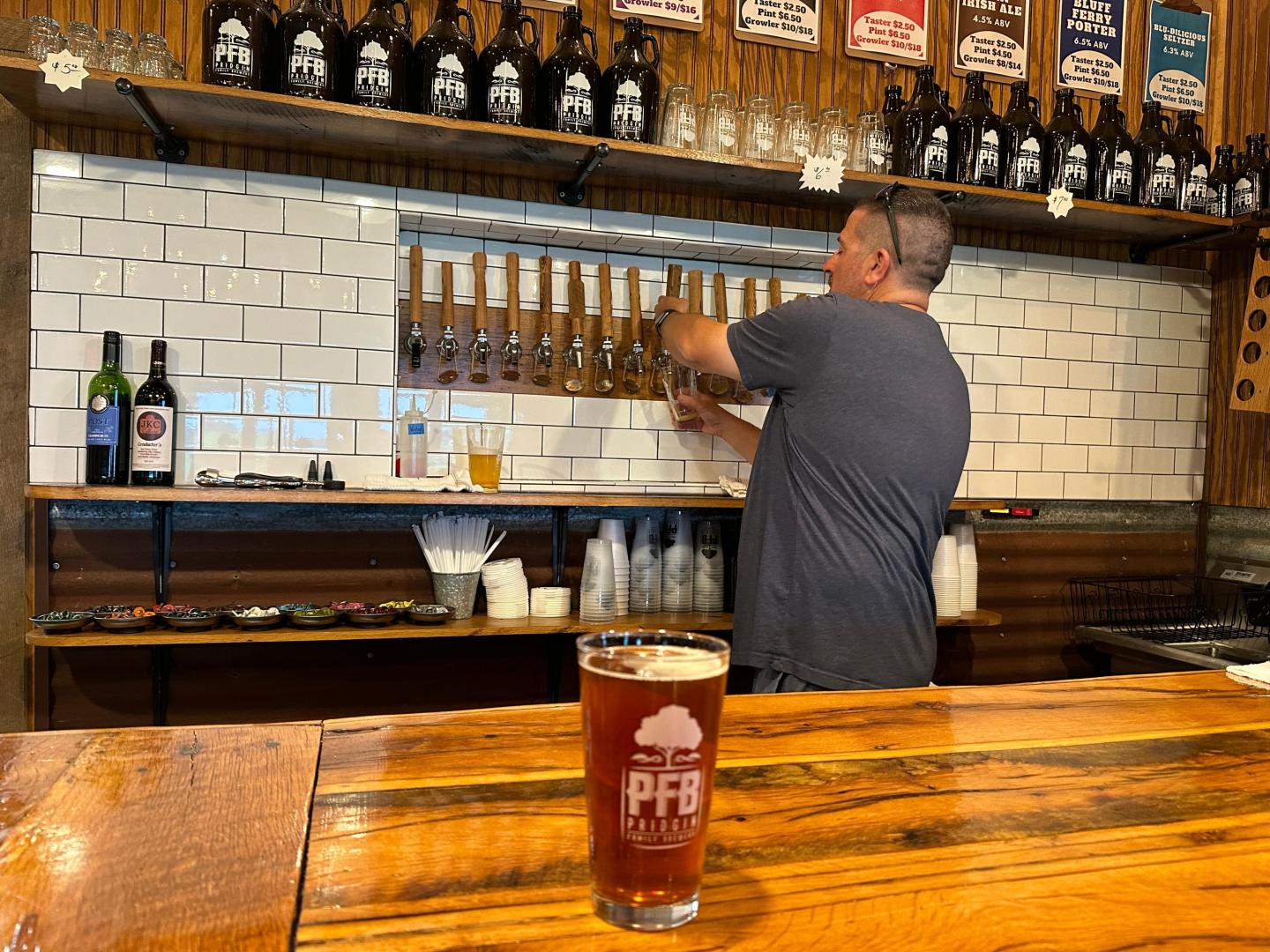 Bartender fills glass at beer tap; a pint on wooden counter.
