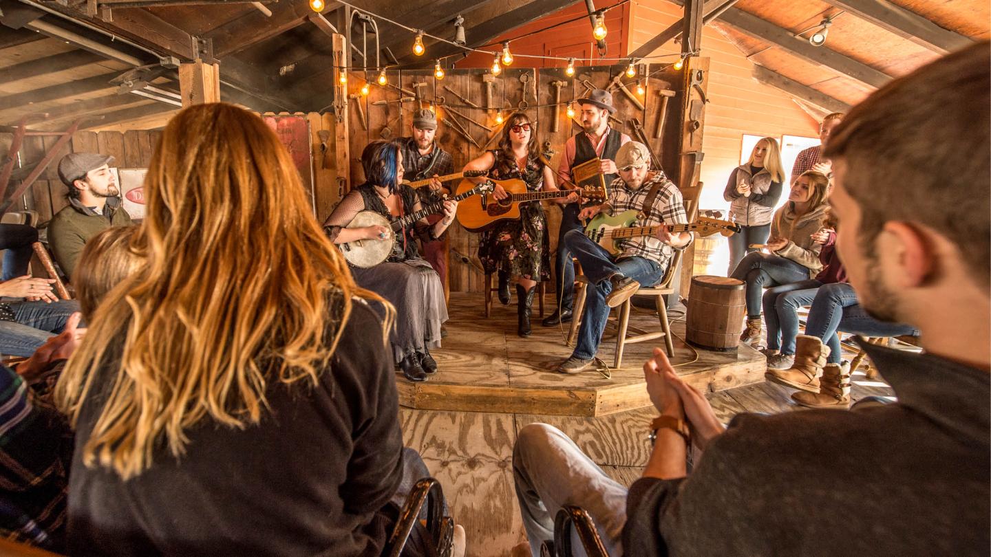 Rustic room with musicians playing string instruments, audience clapping.