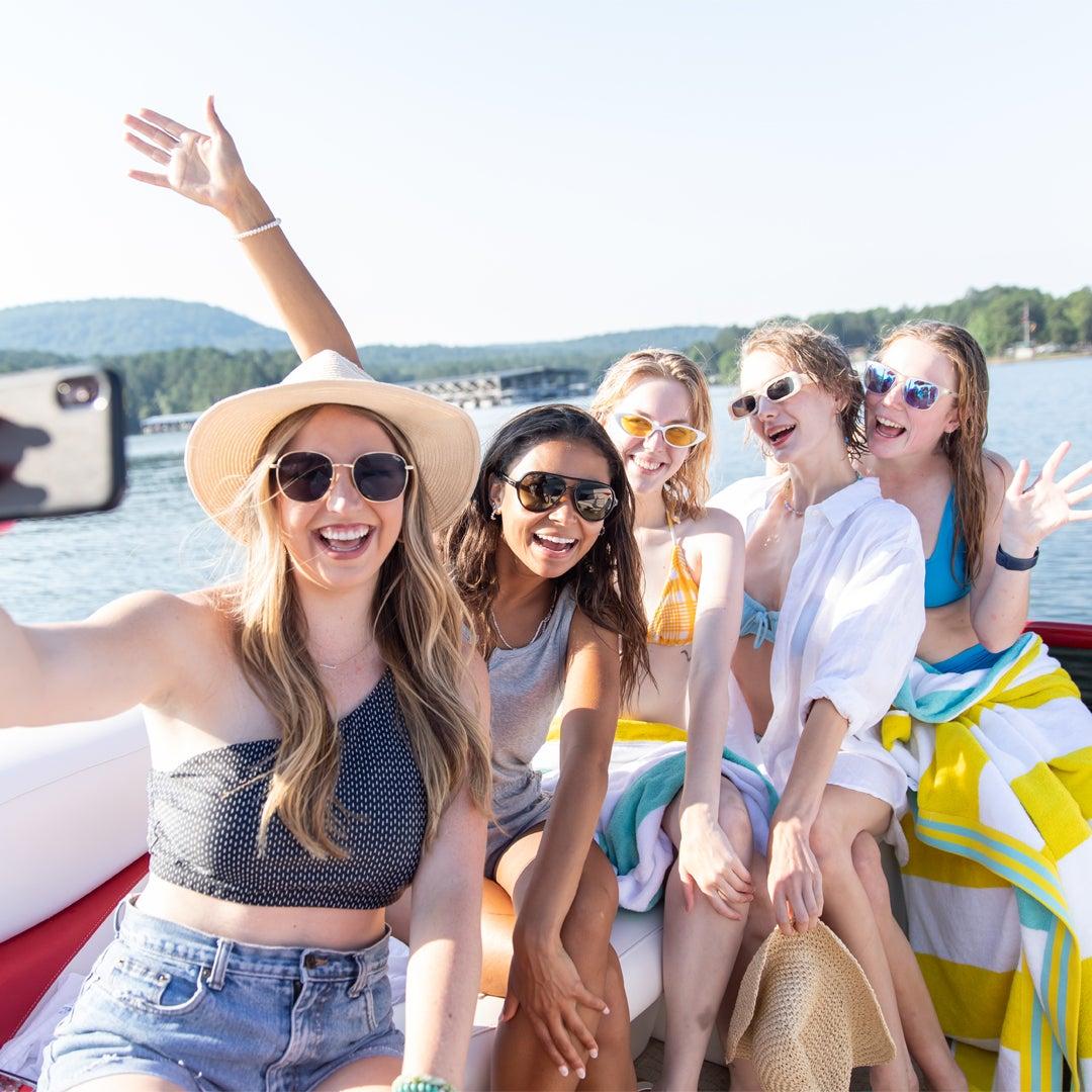 Friends smiling on a boat, posing for a selfie under a clear sky.