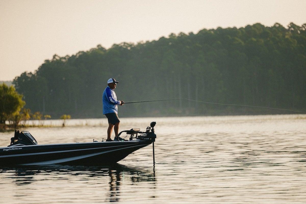 A person fishing on a boat in a calm lake, with trees in the background.