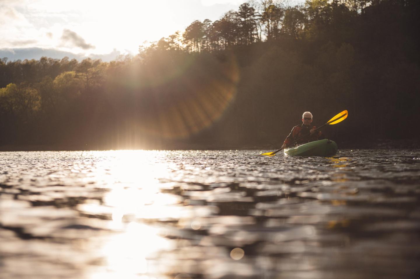 Kayaker paddling on a sunlit lake surrounded by trees.