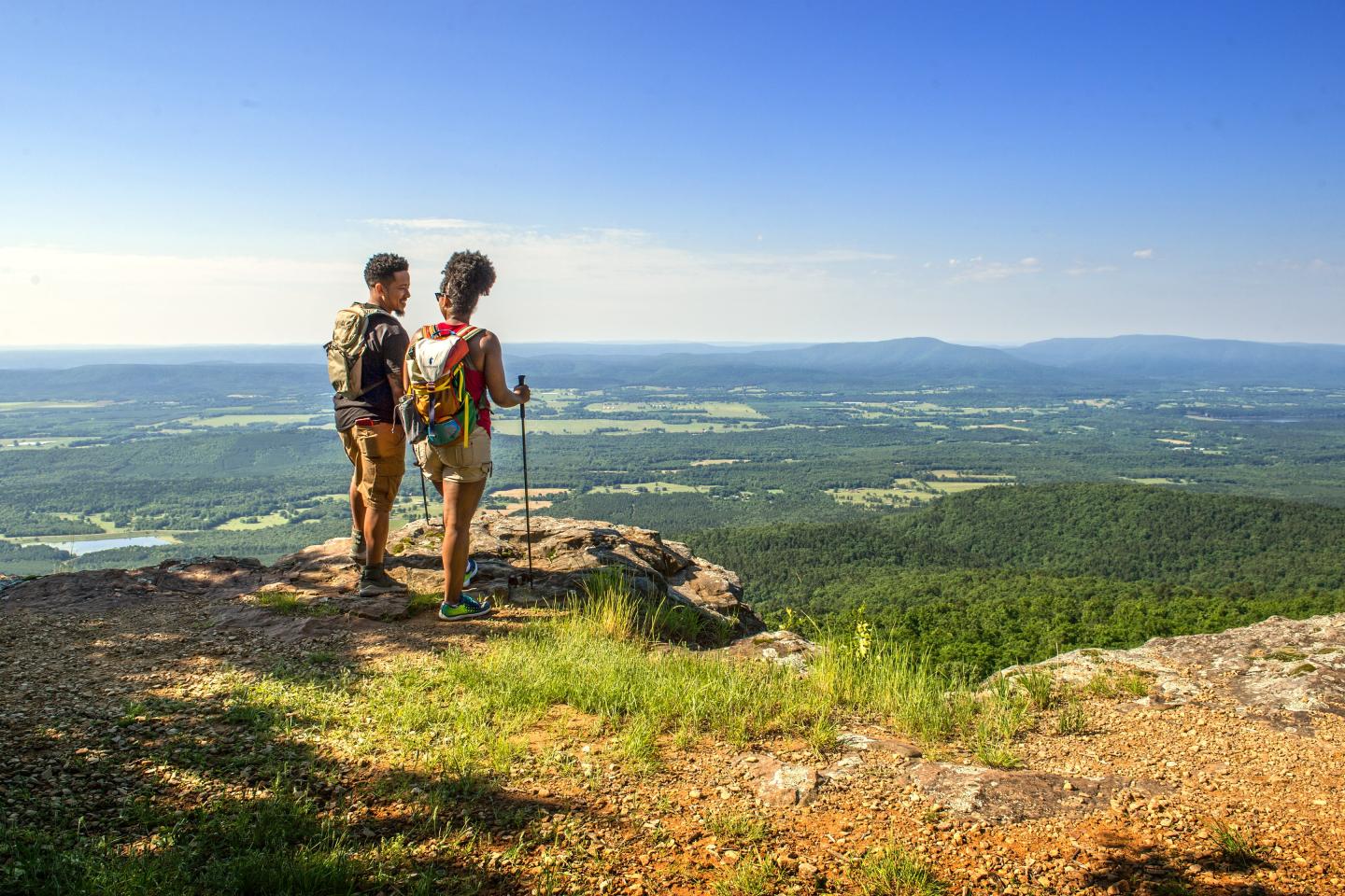 Two hikers with backpacks enjoy a scenic mountain view under a clear blue sky.
