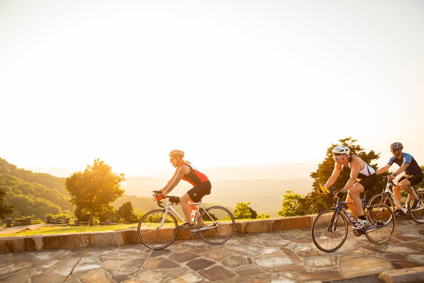 Cyclists riding on a sunny road with distant hills.