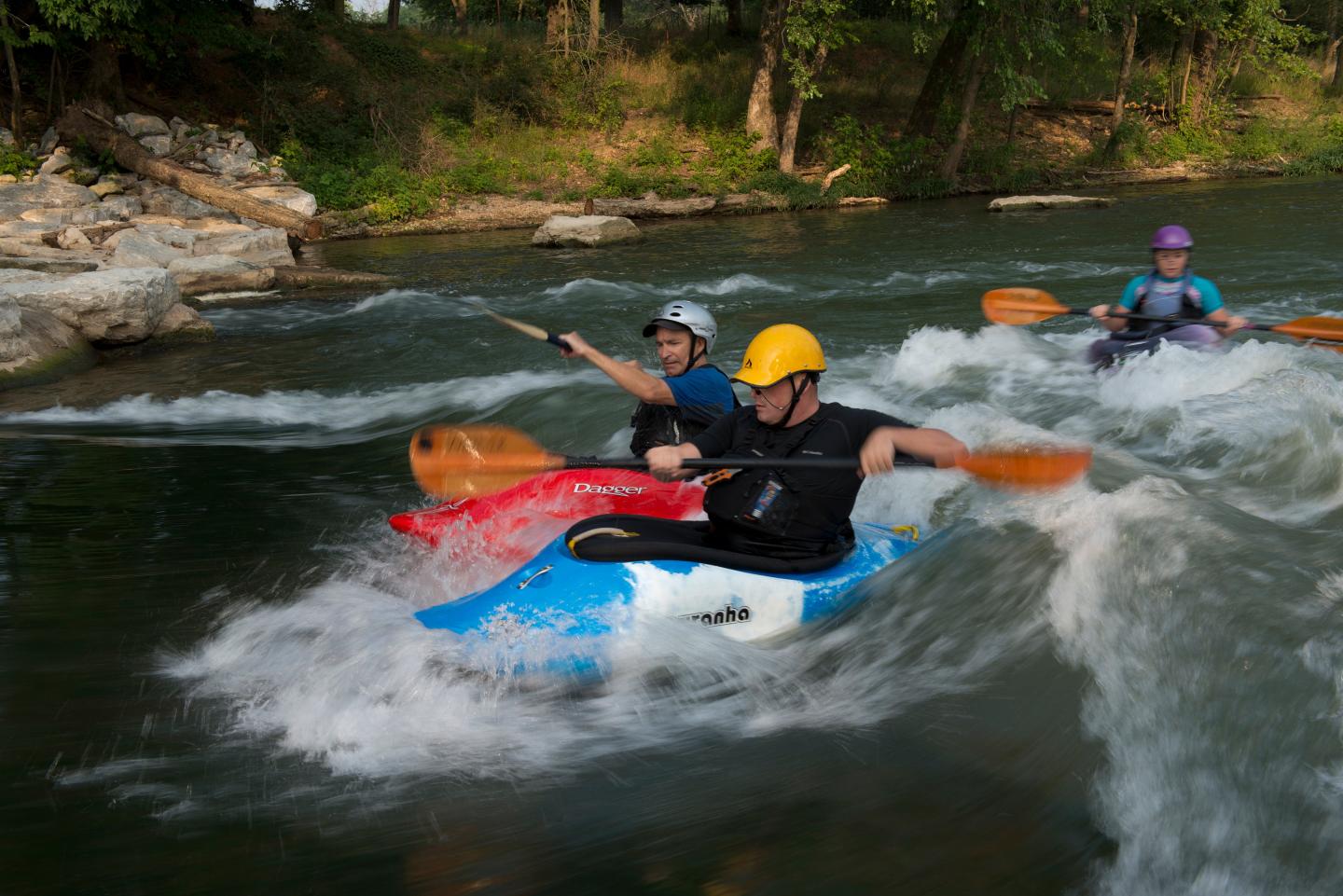Kayakers navigating white water rapids, wearing helmets and life vests.