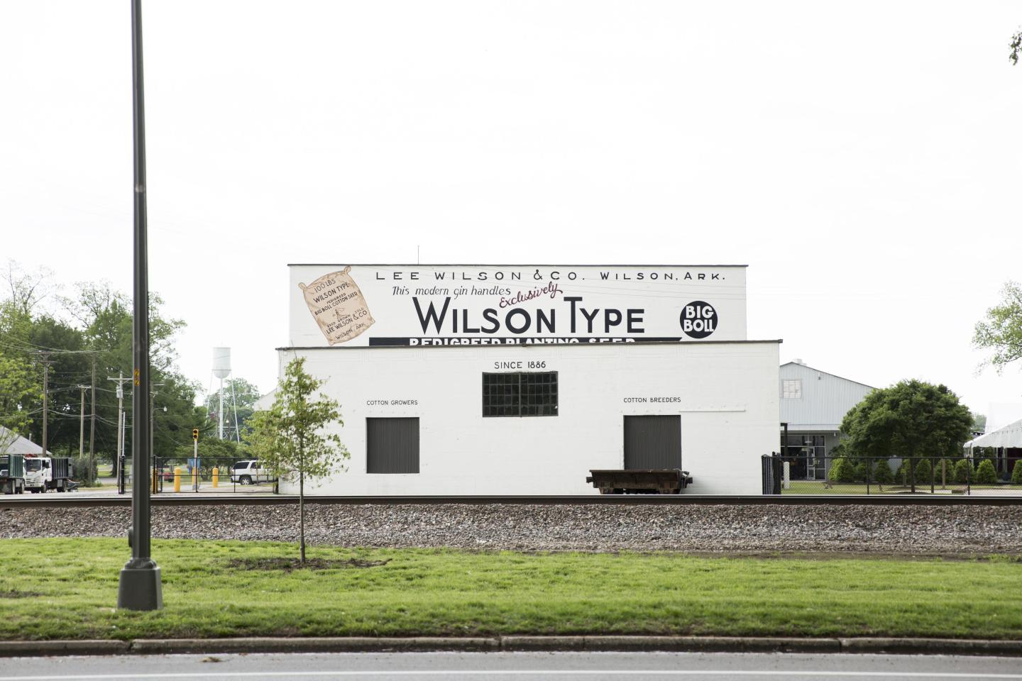 White building with "Wilson Type" sign, railroad tracks in front, trees in background.