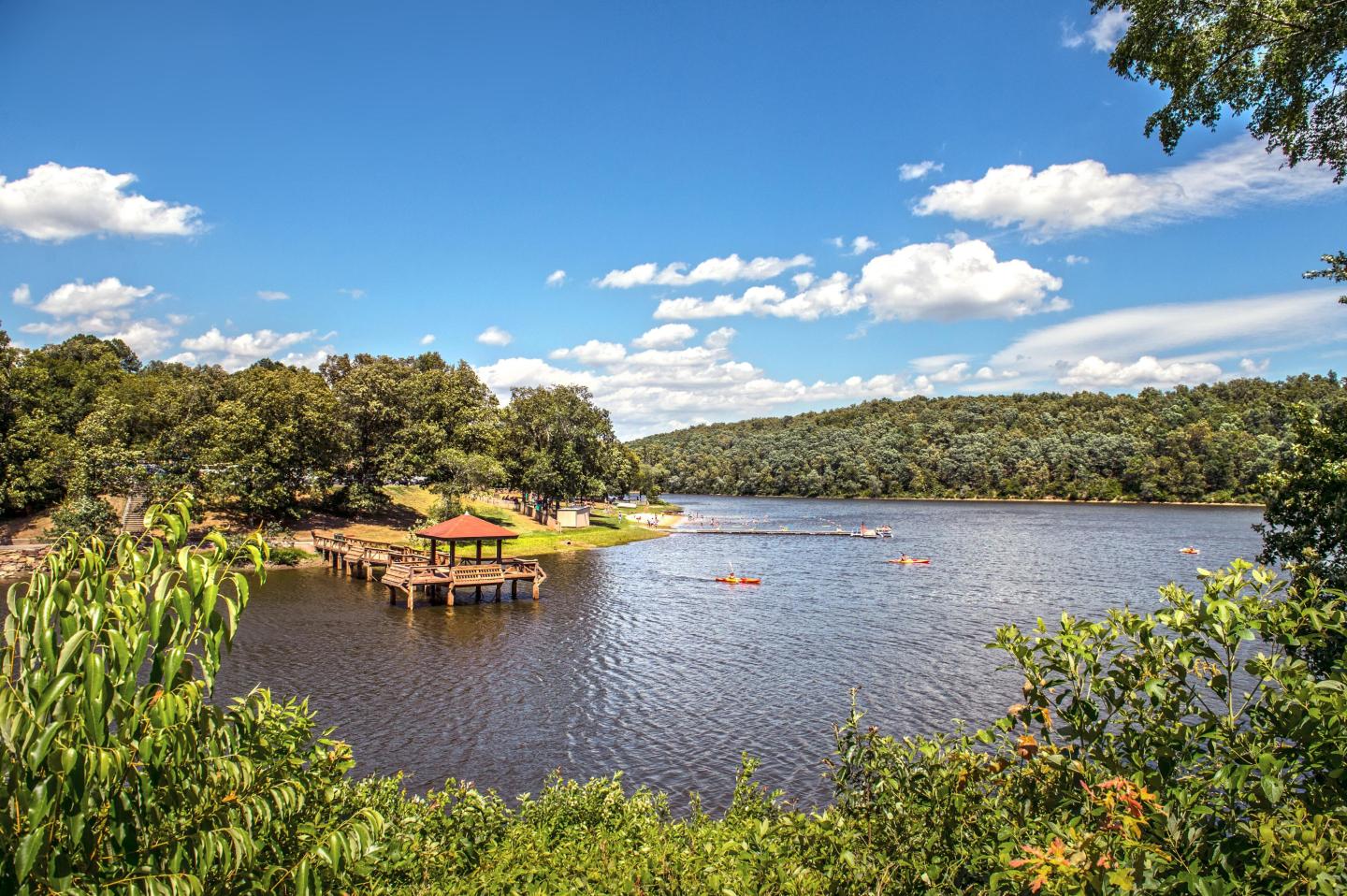 Lake with a gazebo, surrounded by trees under a clear blue sky.