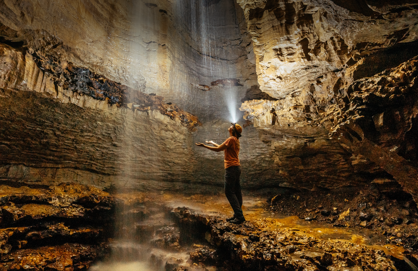 Person in a cave, illuminated by sunlight streaming through the ceiling.