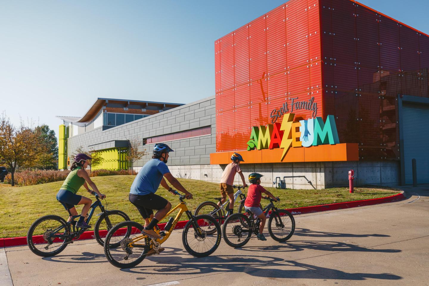 Family biking toward the colorful museum entrance on a sunny day.