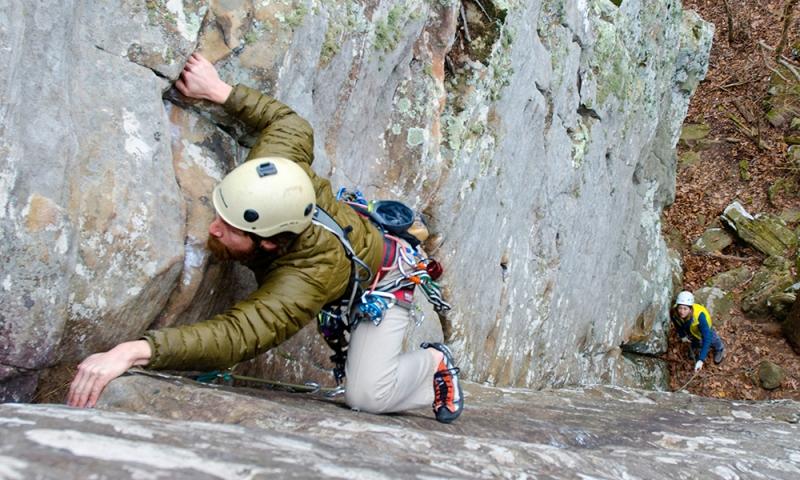 Rock climber in helmet scaling a vertical cliff.