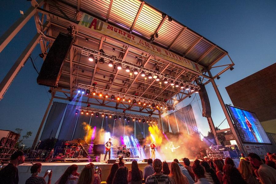 Outdoor concert stage with colorful lights and evening sky.