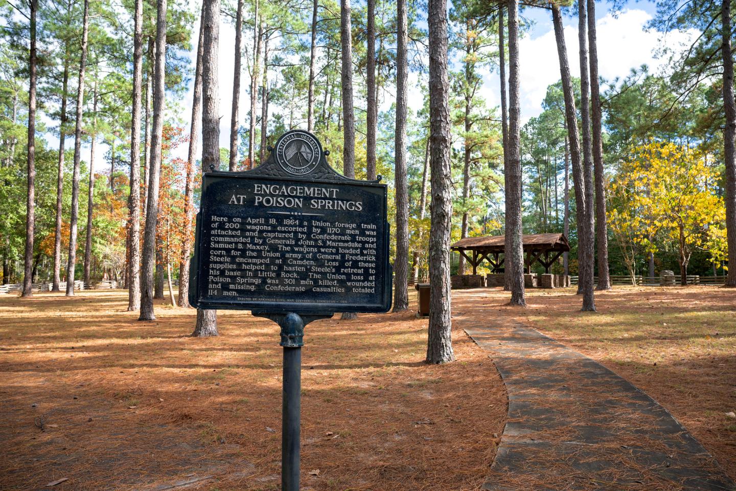 Historic marker in a forested park with a path and pavilion.