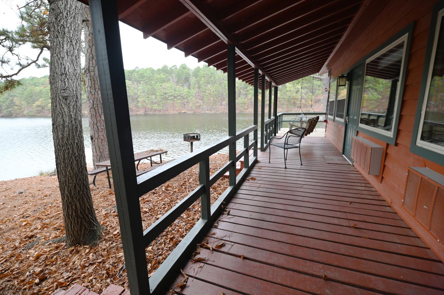 Cabin porch with chairs overlooking a lake and trees.