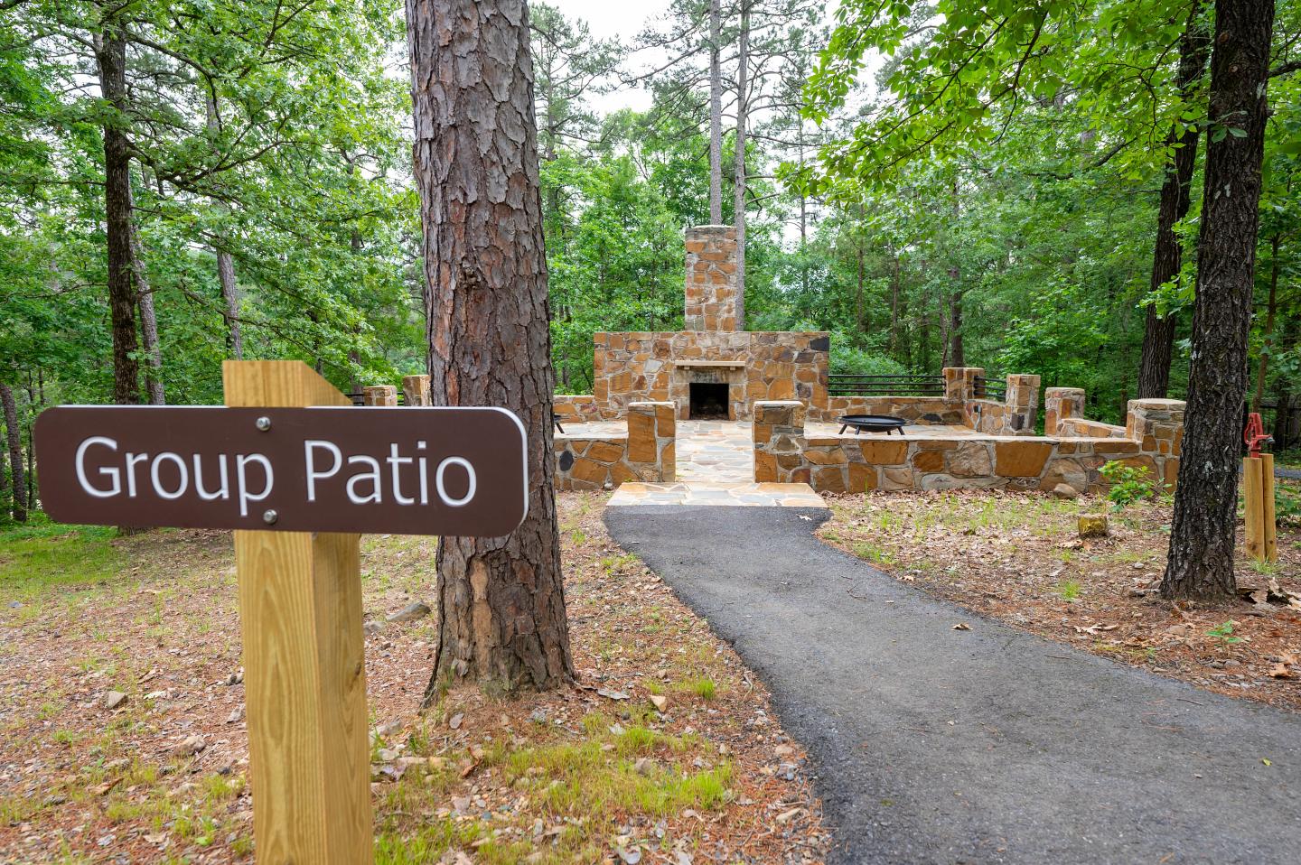 Path leading to a stone patio surrounded by trees, with a wooden sign in the foreground.
