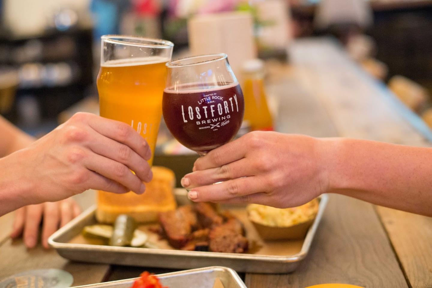 Two hands clinking glasses over a table with food.