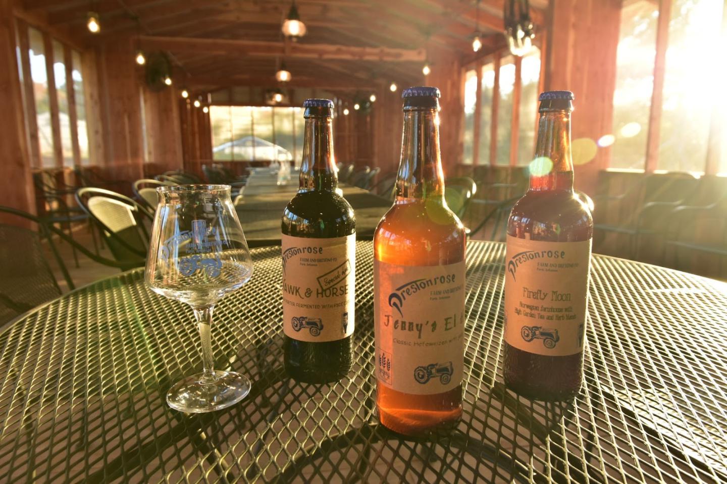 Bottles and a wine glass on a sunlit table in a rustic setting.