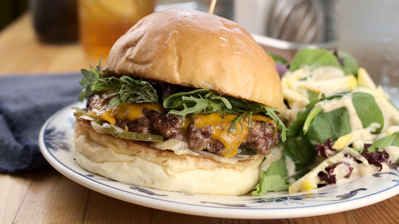 Cheeseburger on a plate with fresh salad, set on a wooden table.
