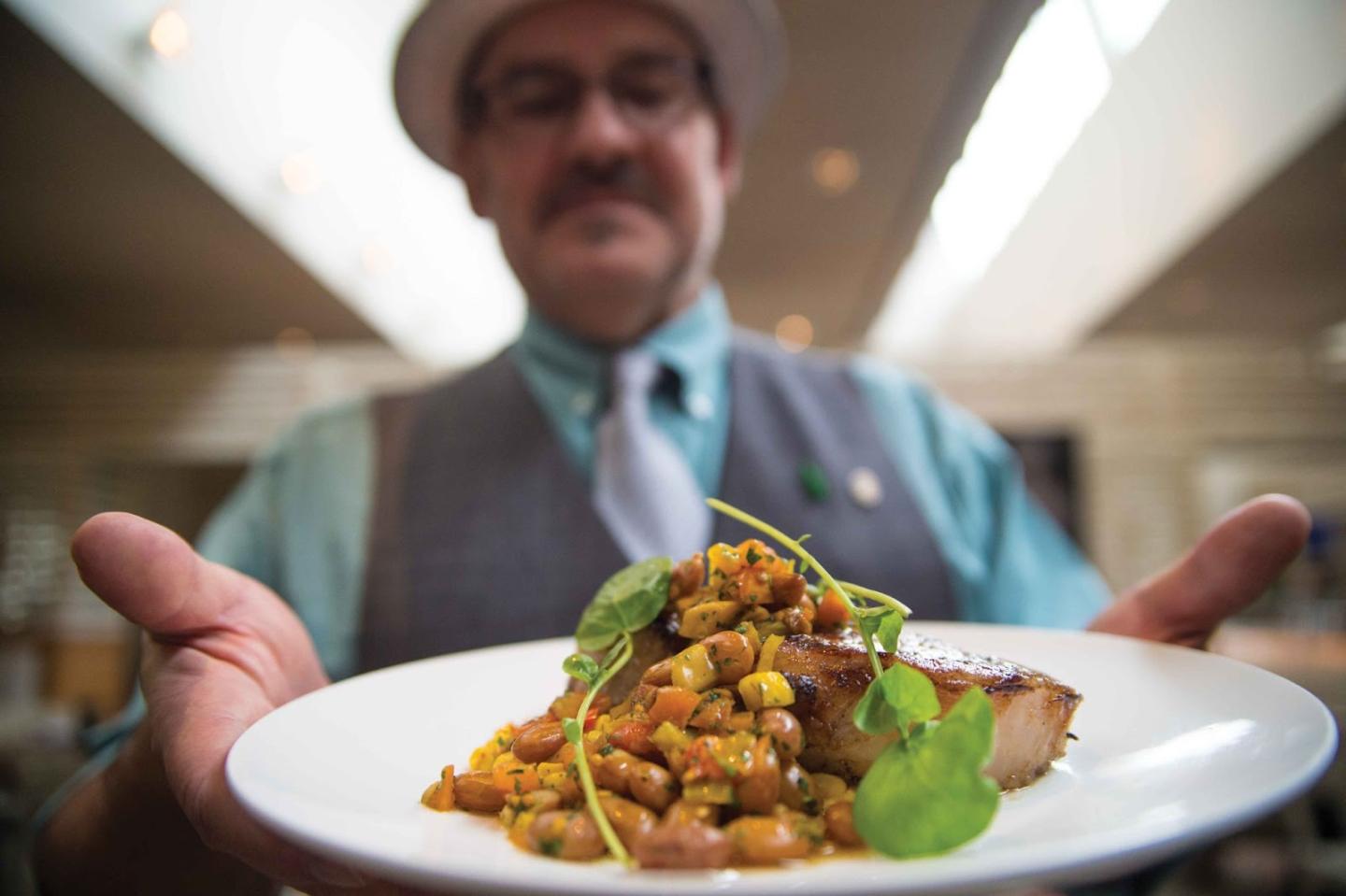 Chef presenting a gourmet dish with herbs on a white plate.