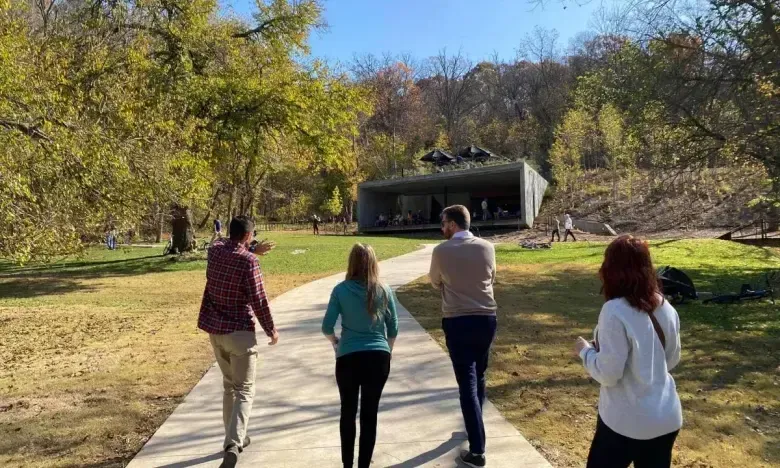 People walk on a sunny path toward a modern black building in a park.