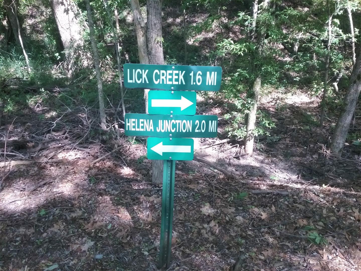 Directional sign in a forest, pointing to Lick Creek and Helena Junction.