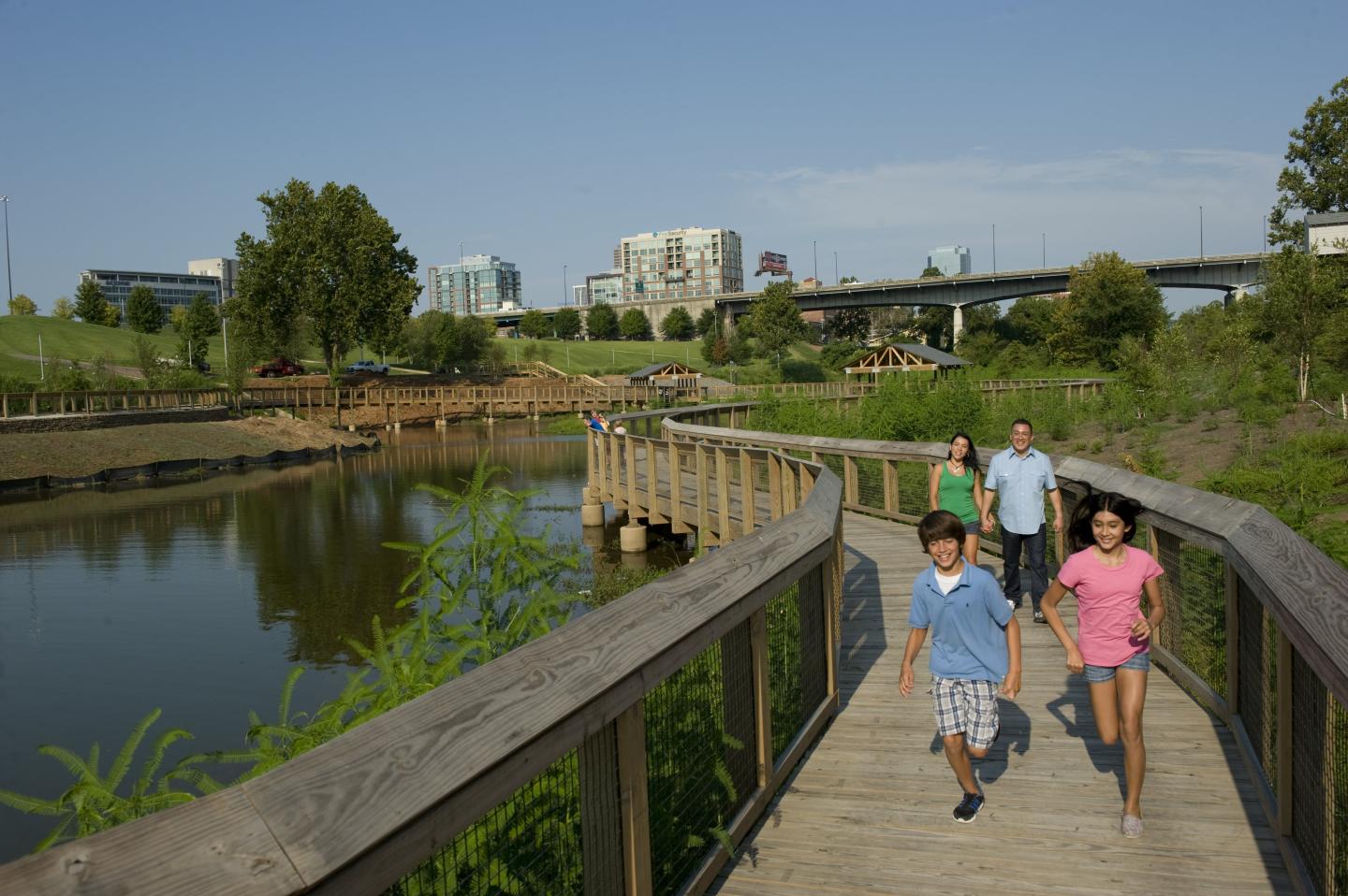 The Bill Clark Presidential Park Wetlands are situated alongside the Arkansas River with views of the Clinton Presidential Center, A family walks down the boardwalk in the Bill Clark Presidential Park Wetlands