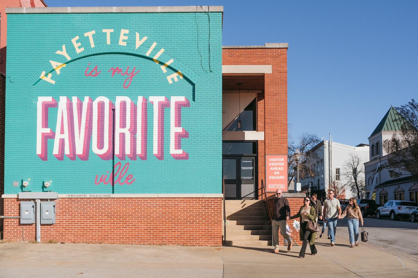Colorful mural reading "Fayetteville is my favorite ville" with people walking nearby.